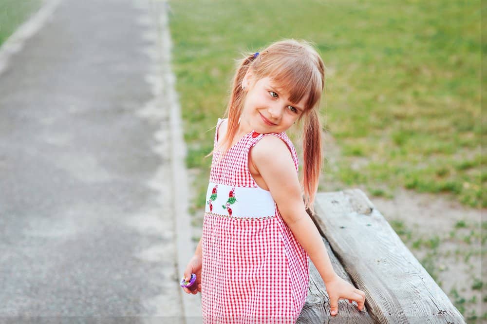 Little smiling girl with two ponytails in red dress posing outside