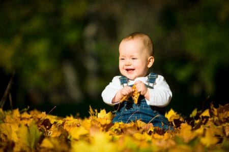Beautiful baby girl sitting and playing in fallen leaves