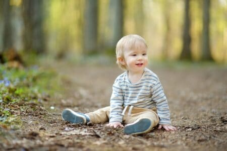 Adorable blonde toddler boy sitting on the ground having fun in the woods