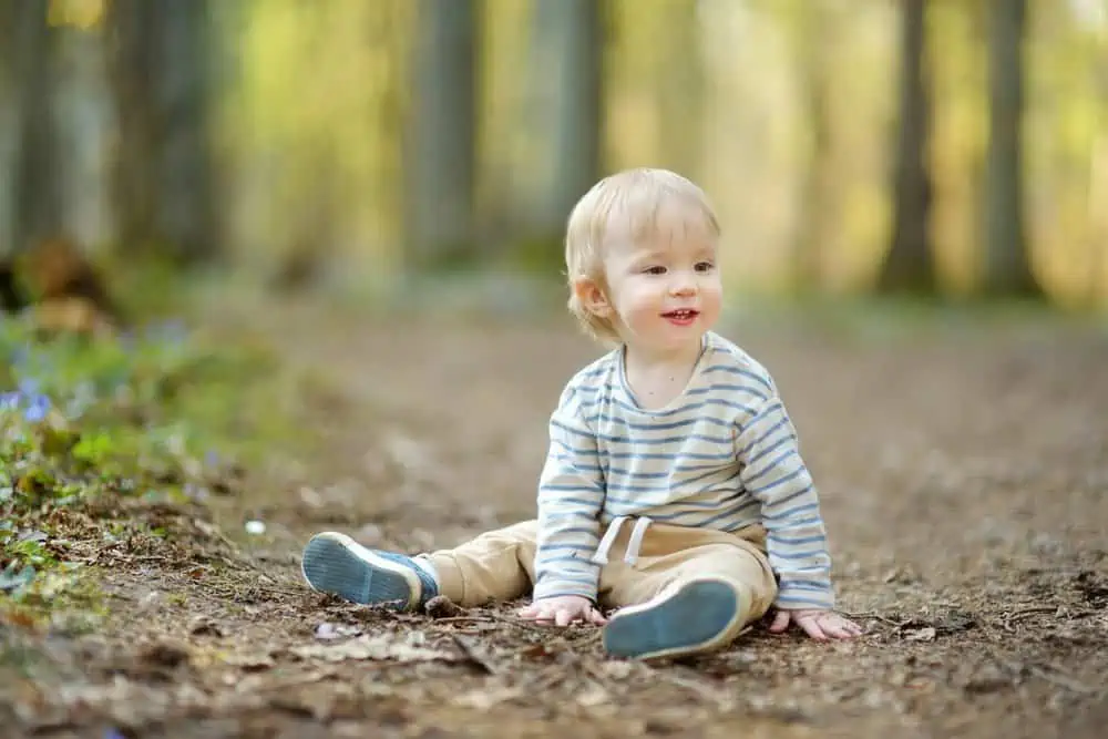 Adorable blonde toddler boy sitting on the ground having fun in the woods