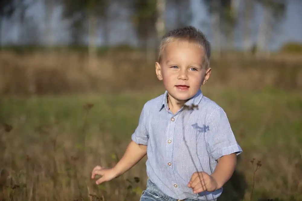 Handsome little boy with blond hair wearing polo shirt playing in the field