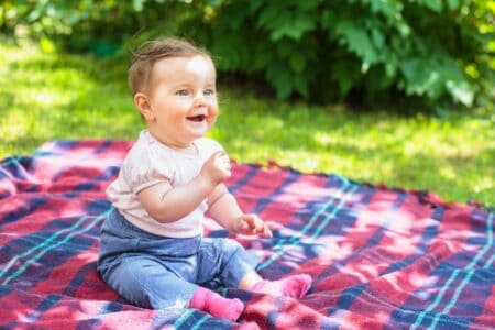 Cheerful little baby girl sitting on plaid blanket in a garden