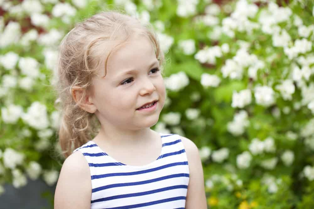 Adorable little girl in ponytail standing in the garden with white flowers