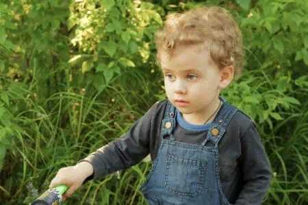 Cute little blond boy wearing denim overall in the garden on sunny day