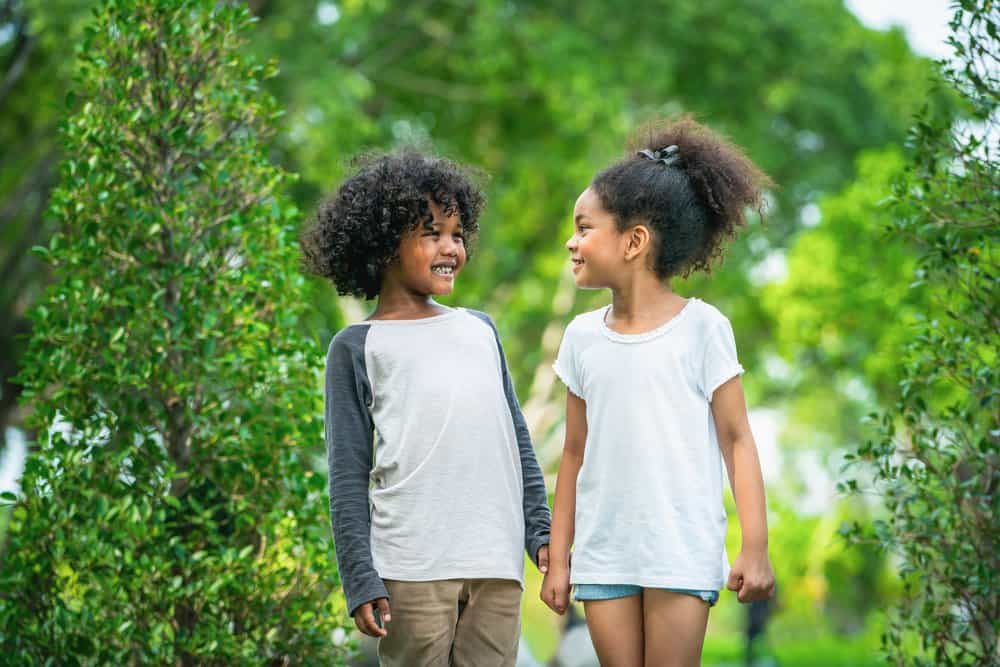 Two african american kids walking in the garden smiling brightly at each other