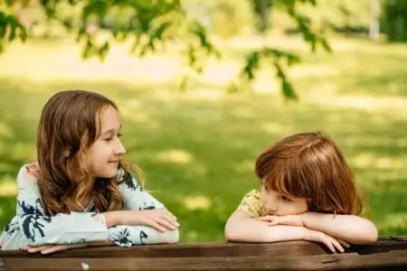 Little young boy with long hair and pretty girl sitting on park bench