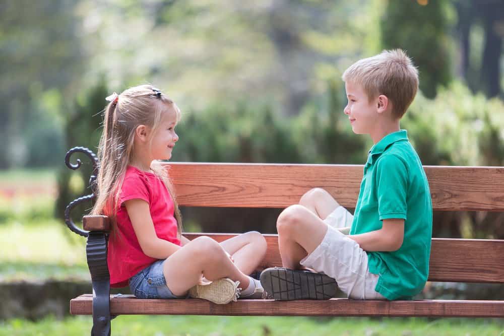 Cute young boy and girl having fun time on bench in summer park outdoors