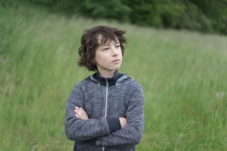 Black haired young boy with proud look wearing jacket standing in green meadow