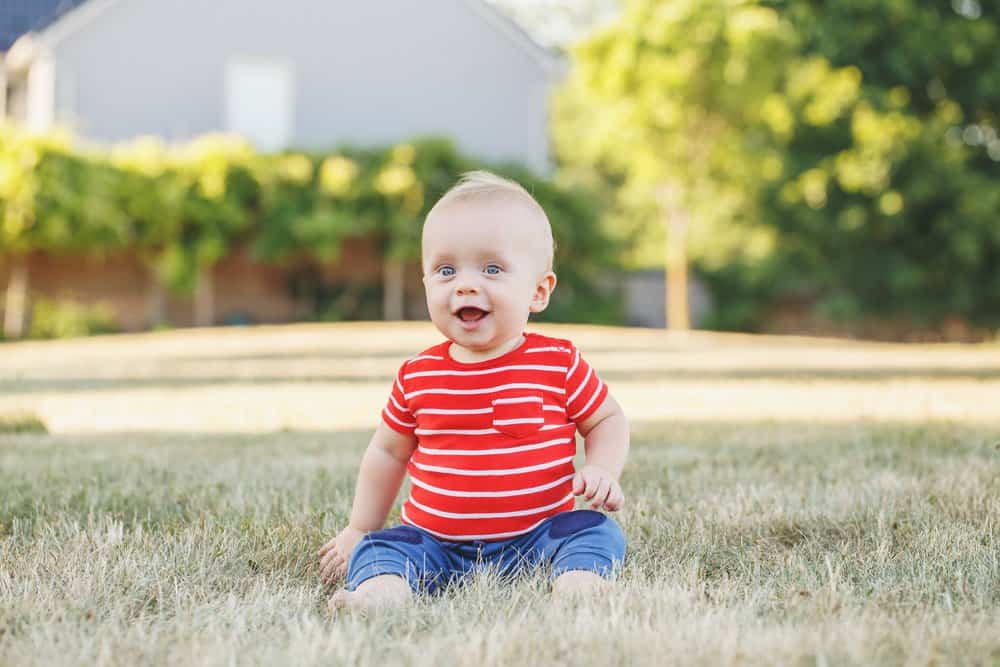 Cute little boy in red t-shirt sitting on the ground outdoors