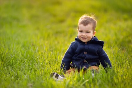 Little boy in blue cardigan sitting on the grass