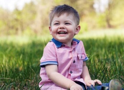 Happy little boy in a pink shirt sitting on the grass in the park