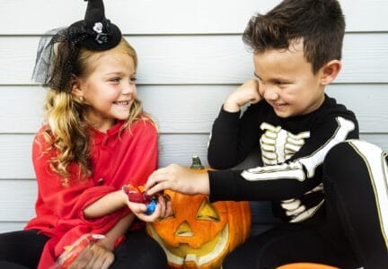 Little girl and boy dressed in Halloween costumes give each other candy
