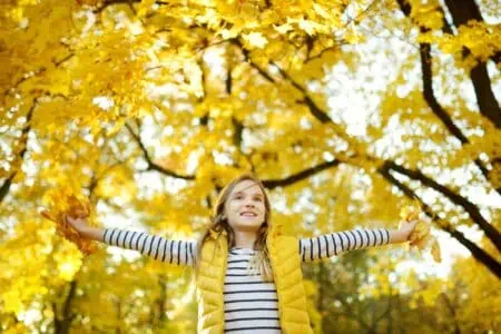 Happy little girl playing with yellow leaves in the park