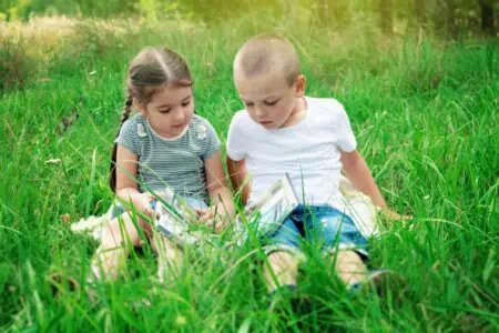 A boy and a girl reading a book while sitting on the grass in the park