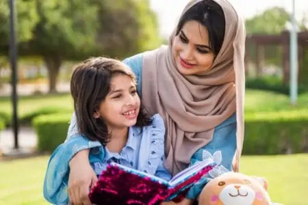 A Muslim mother reading a book with her daughter in the park