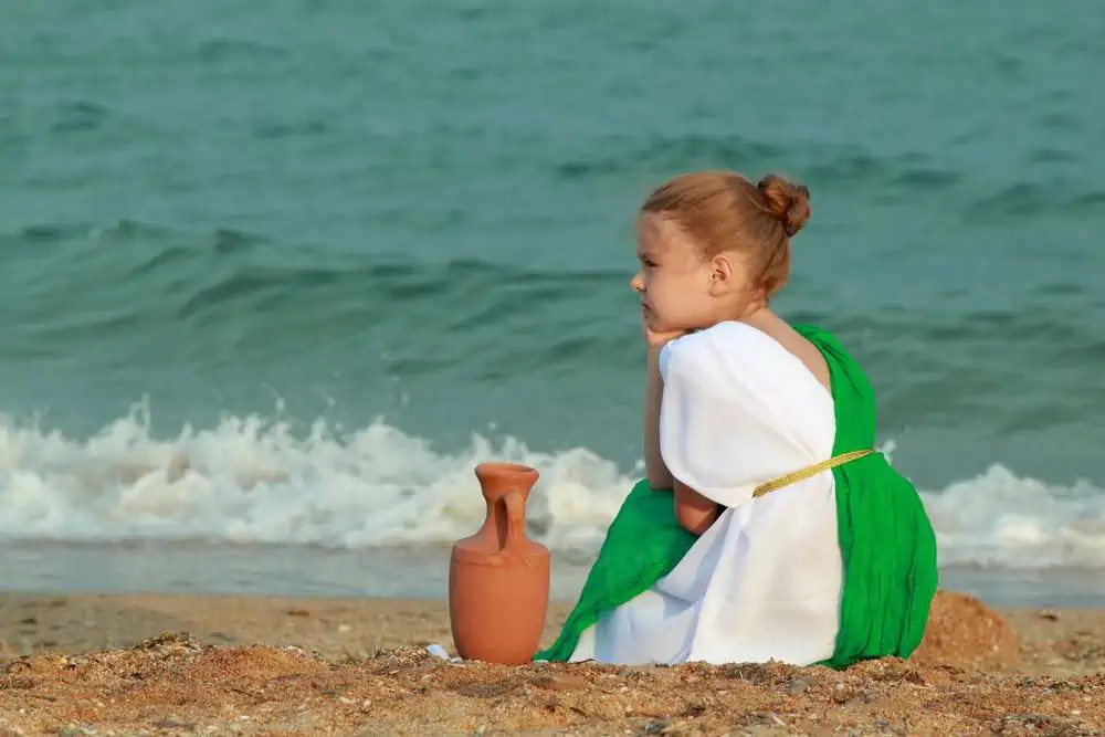 Little Roman girl with amphora sitting on the sea shore.