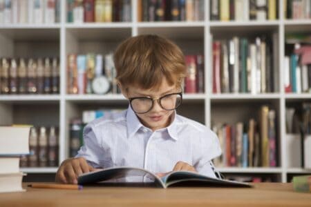Little boy in glasses reading a book in the library.