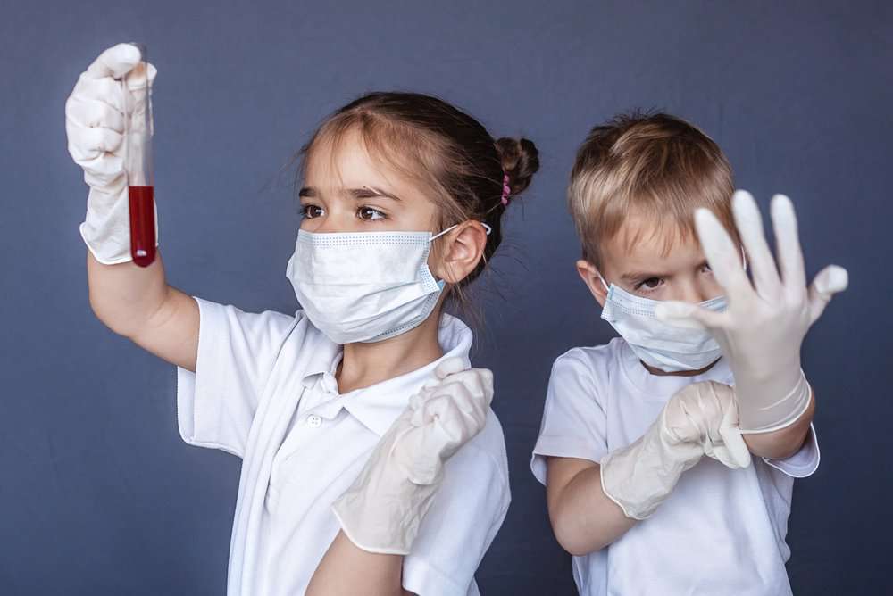 Kids dressed as doctors looking at a glass blood collection tube.