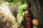 Little girl dressed as a witch holding a broom and a pumpkin in her hands.