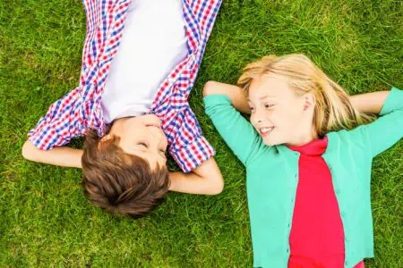 A boy and a girl looking at each other while lying on the grass.