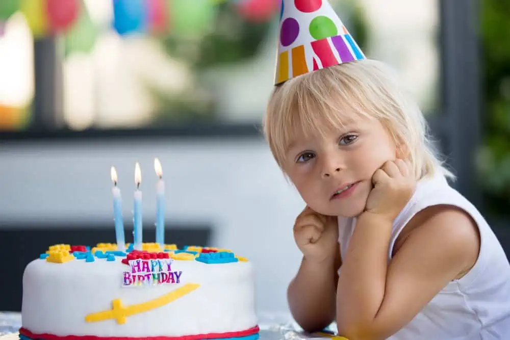 Little girl sitting next to the third birthday cake.
