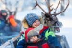 A mother and her son having fun during a reindeer sleigh ride.