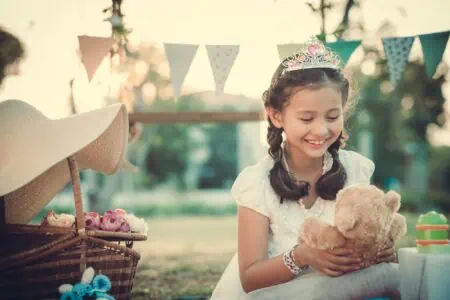 Little girl dressed as a princess playing with a teddy bear.