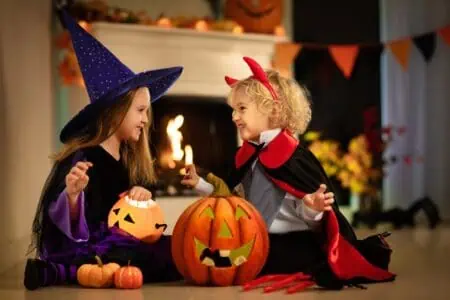 Little girl wearing a witch costume and a boy dressed as a vampire playing near the fireplace.