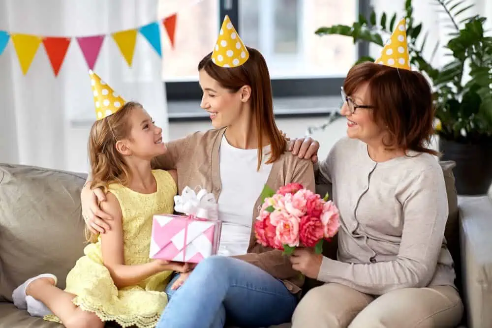 Little girl receiving a present on her 7th birthday from her mother and grandma.