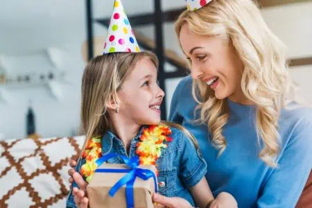 Girl receiving a present on her 8th birthday from her mother.