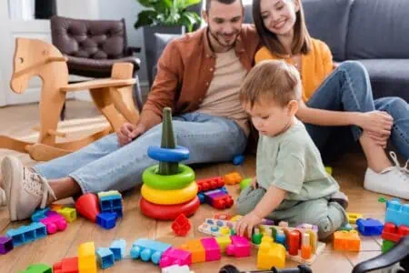 Parents looking at their son playing with toys.