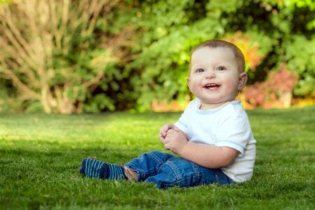 Smiling little boy sitting on the grass in the park.