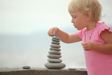 Little girl in a pink dress stacking pebbles.