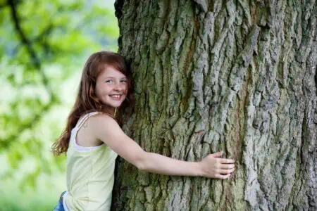Happy little girl hugging a tree.