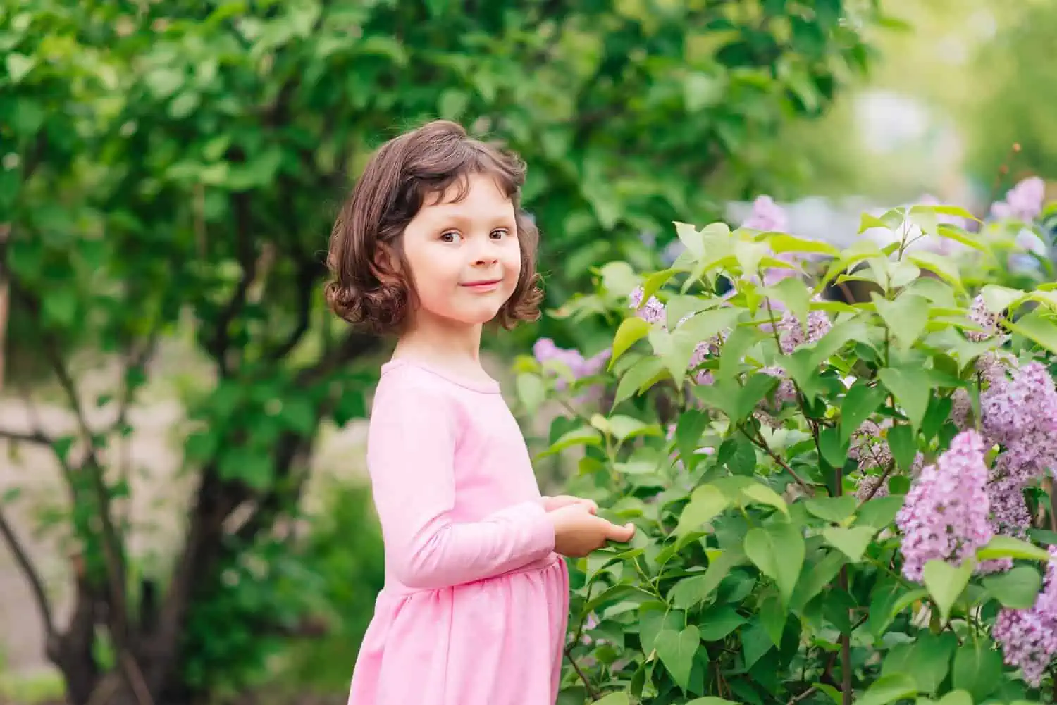 Adorable short haired girl in pink dress having fun in the garden looking at the camera