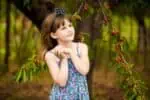 Cheerful young girl in dress standing near cherry tree in summer garden