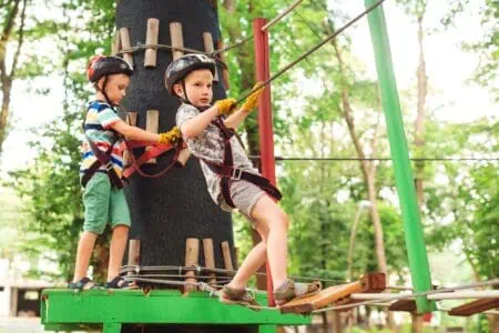 Brave young boys in safety helmets passing through high tree rope in adventure park