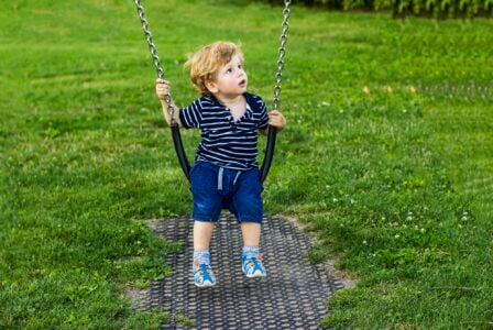 Cute blonde boy on swing in the park