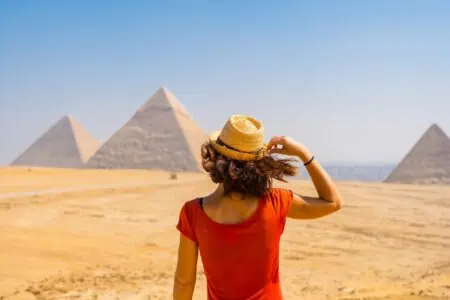 Egyptian girl in red shirt and straw hat looking at the pyramid from afar