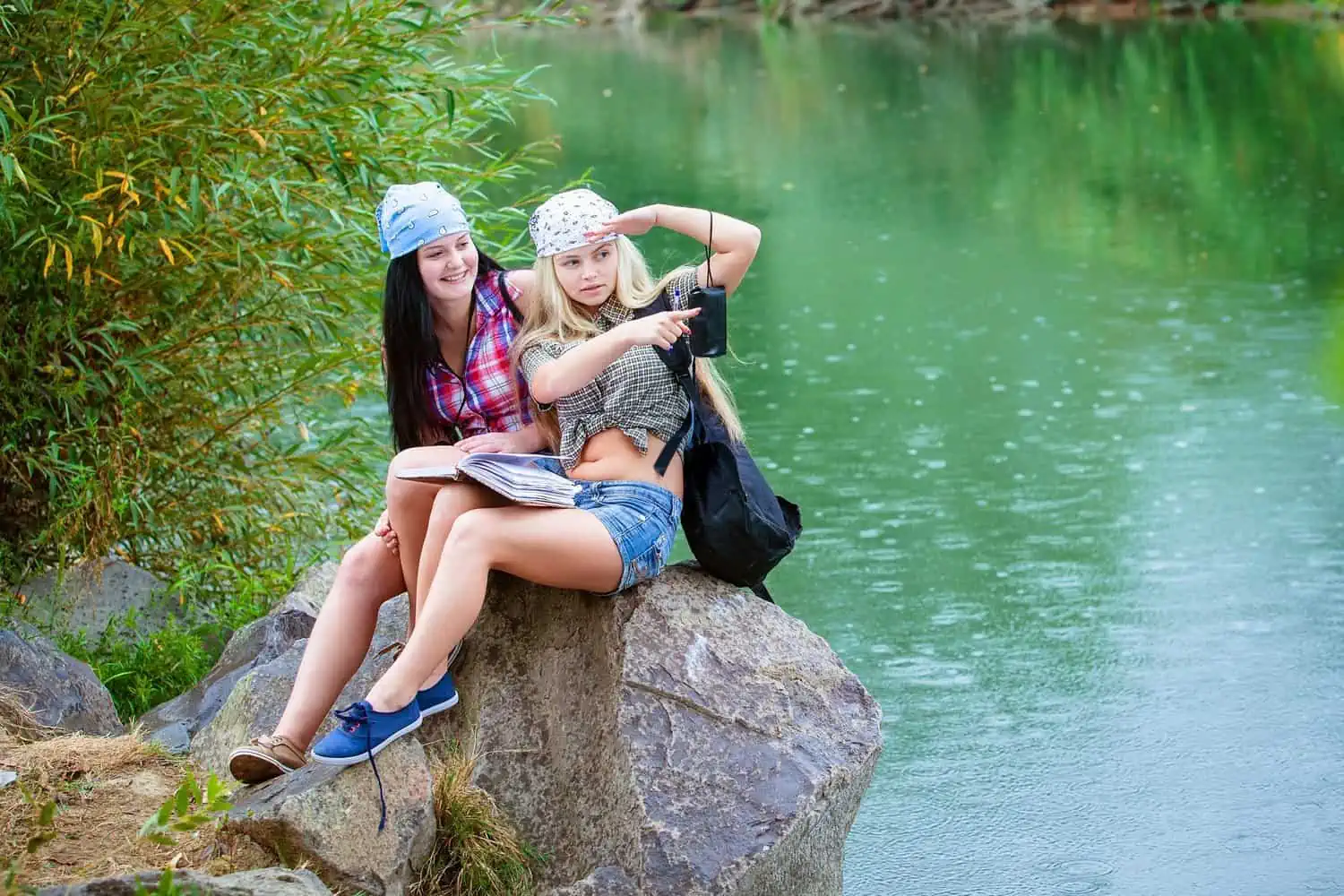 Two females wearing bandanas sitting on rock near the river