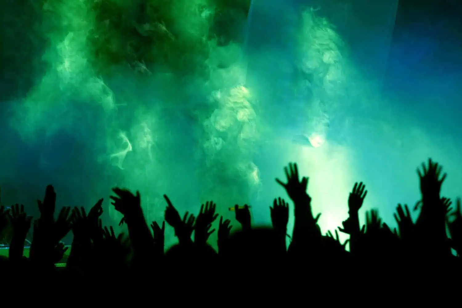 Party people raising their hands on concert with green stage lighting