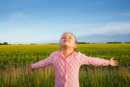 Smiling little girl with extended arms in front of canola field
