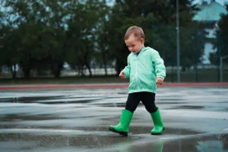 Little boy wearing green raincoat and boots playing outside after the rain