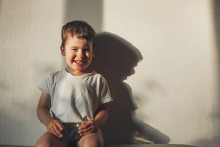 Cute toddler boy sitting on the couch against the wall with his shadow