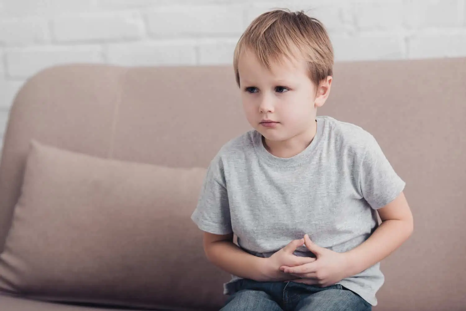 Young boy having constipation sitting on sofa