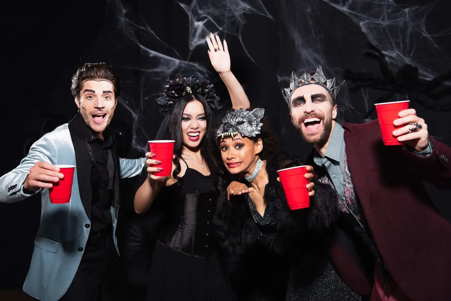 Teenagers with spokky costumes holding red cup against black background