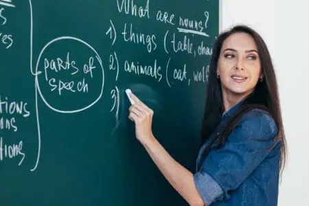 Female professor in denim top writing on chalkboard teaching nouns