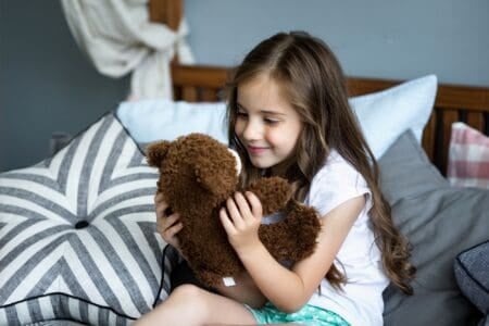 Cute little girl playing with toy bear on the bed