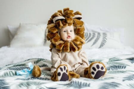 Adorable little girl wearing lion costume sitting on the bed