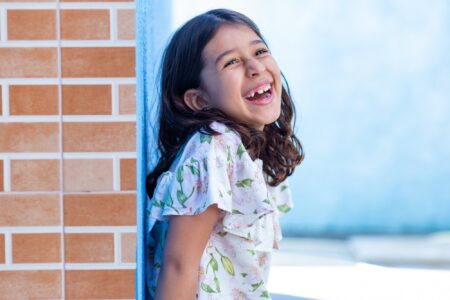 Puerto rican little girl leaning on brick wall smiling brightly